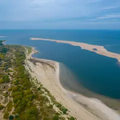 Piaszczysta wyspa na Bałtyku, otoczona wodą i zielenią, tworzy malowniczy krajobraz.