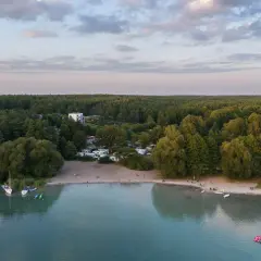Widok na kemping nad najczystszym jeziorem w Polsce. Woda jest turkusowa, a brzeg piaszczysty. W oddali las.