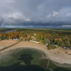 Jesienny krajobraz nad Skorzęcinem. Tęczowy łuk nad jeziorem i plażą, otoczone kolorowymi lasami.