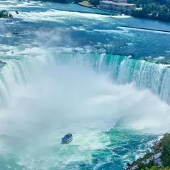 Potężny wodospad Niagara w całej okazałości. Widać łódź turystyczną i tłumy ludzi podziwiających ten cud natury.