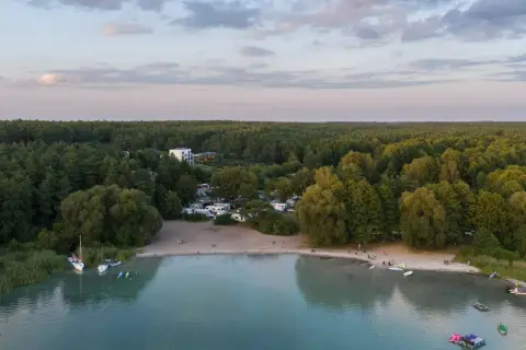 Widok na kemping nad najczystszym jeziorem w Polsce. Woda jest turkusowa, a brzeg piaszczysty. W oddali las.