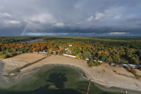 Jesienny krajobraz nad Skorzęcinem. Tęczowy łuk nad jeziorem i plażą, otoczone kolorowymi lasami.