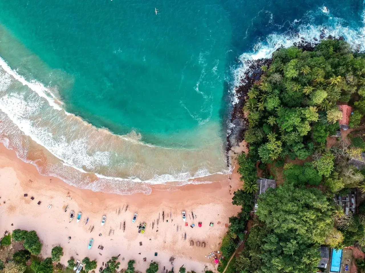 Rajskie Sri Lanki plaże z turkusową wodą, piaszczystym brzegiem i łodziami. Tropikalna zieleń otacza zatokę.